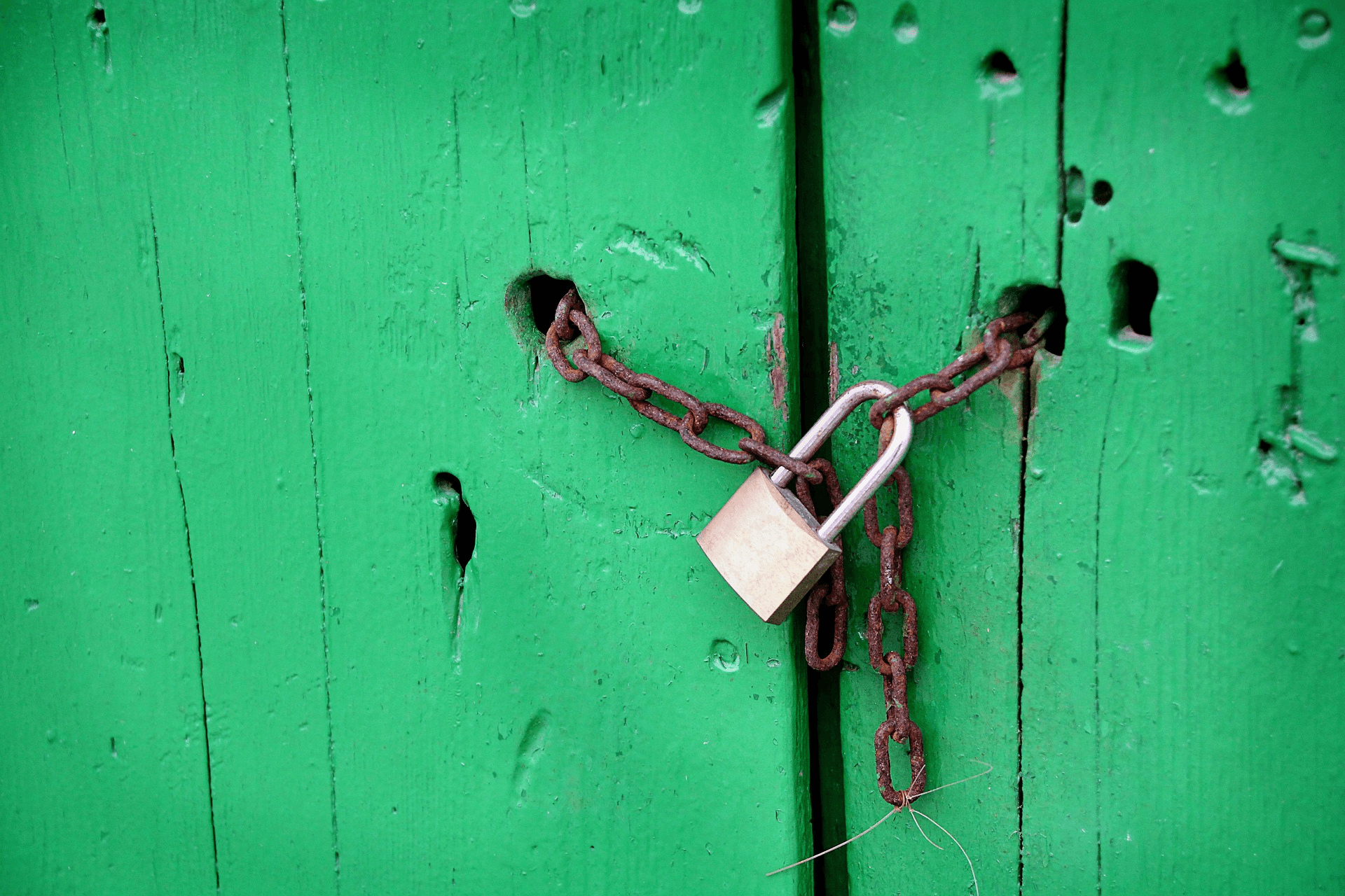 A lock on a chain securing a green wooden door.