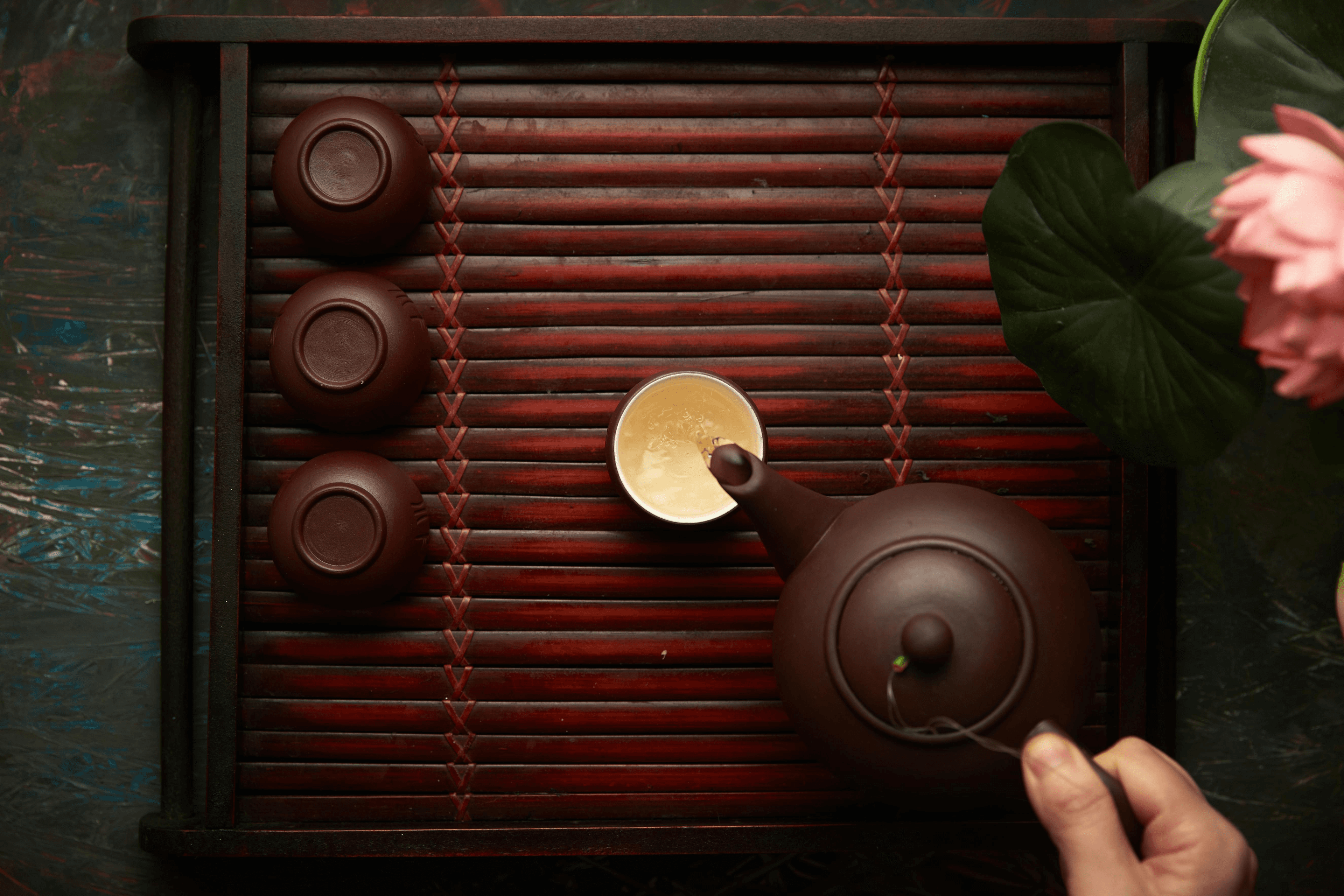 A hand pouring tea from a vintage japanese into a cup.