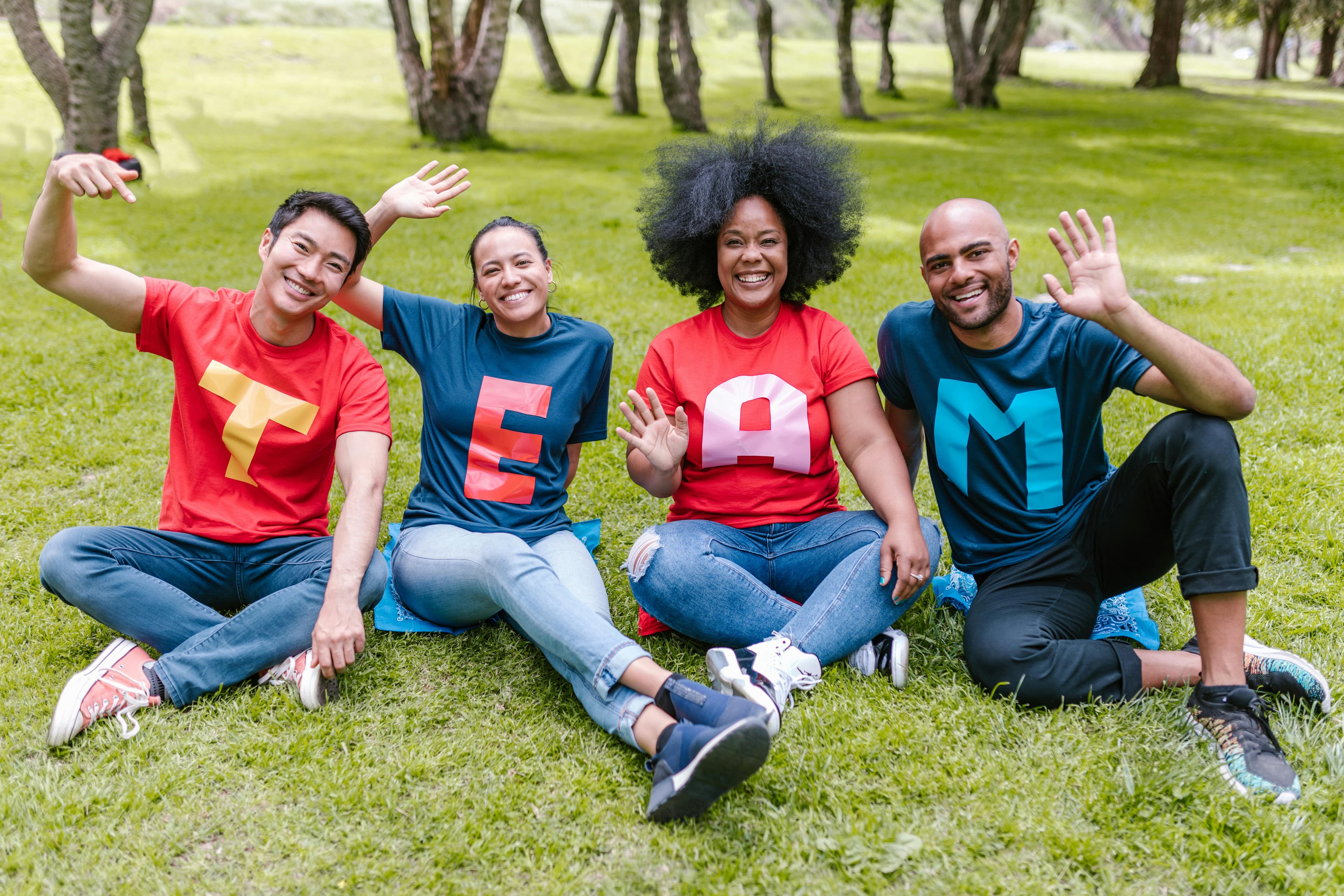 A group of people sitting in a park with each the letters of TEAM on their shirt.